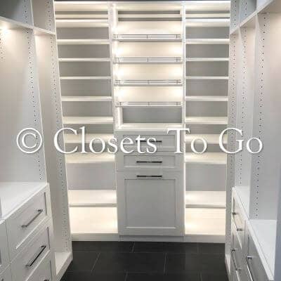 Walk in white led closet with drawers and tilted shelves.