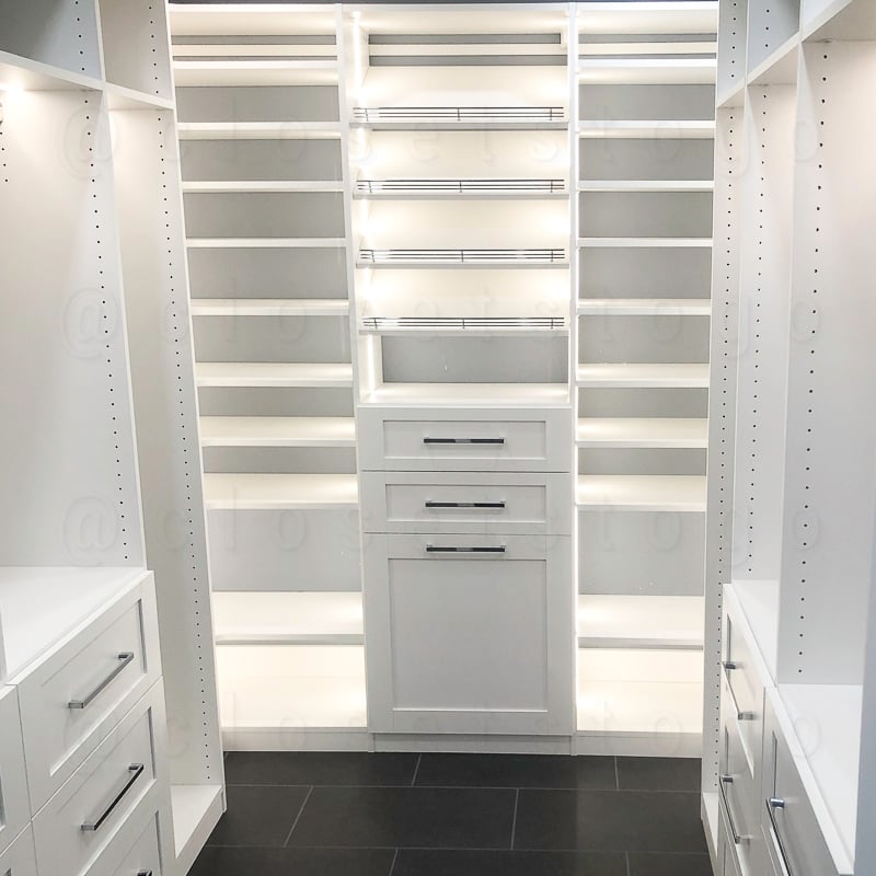 Walk in white led closet with drawers and tilted shelves.