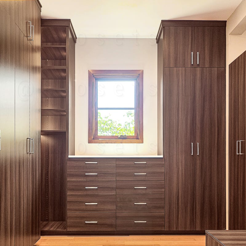 Brown walk in spacious closet with tall closed drawers and closed doors, open window.