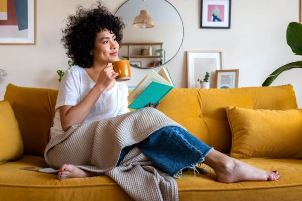Lady on a couch with a cup and a book