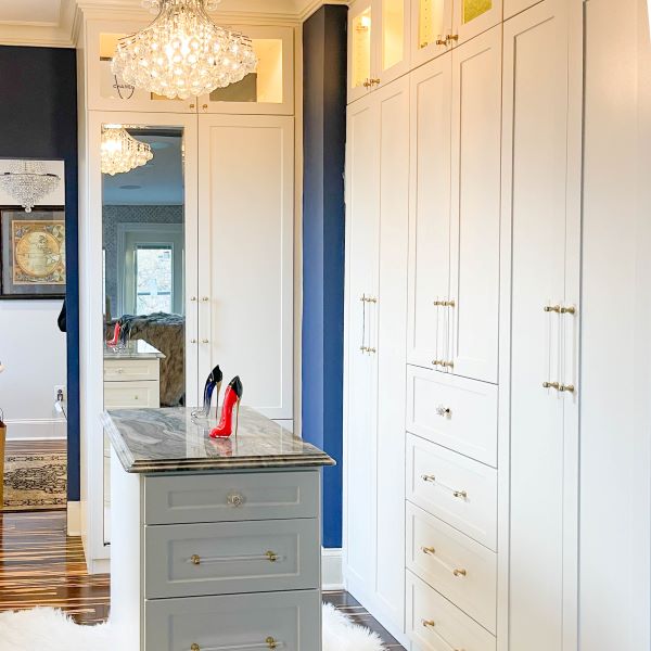 A Luxury White Closet with a island in the center, several drawers and long doors for long hang.