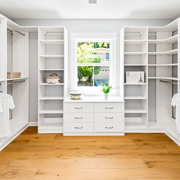 A Luxury White Closet with a medium sized window in the center, several shelves to the left and right of the window. Including some medium hangs.
